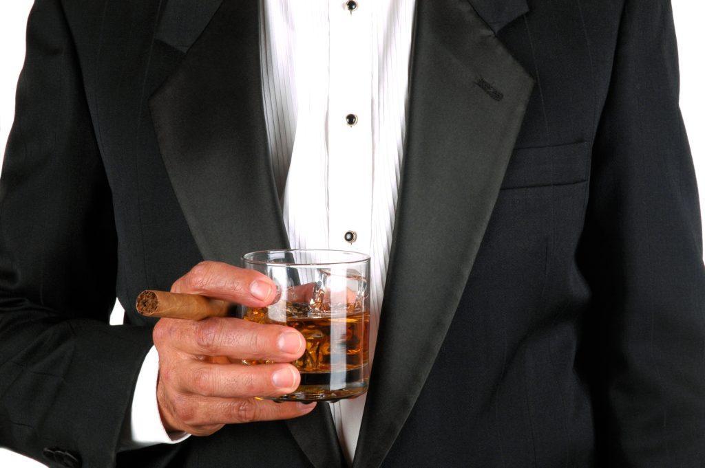 Man in a tuxedo holding a whiskey glass and cigar, evoking classic spy style